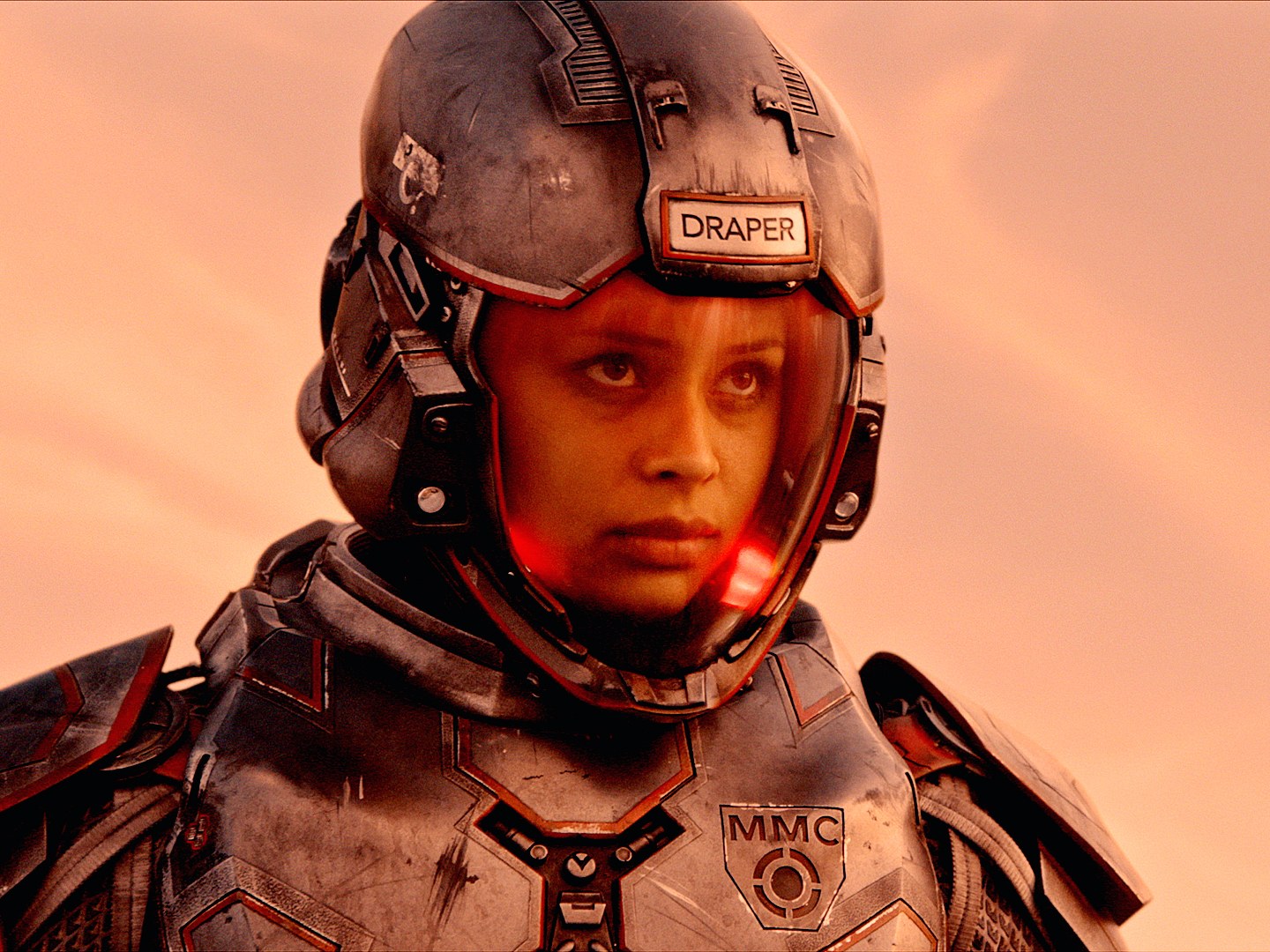 The Image shows the a woman in spacesuit, behind her is a slightly red sky